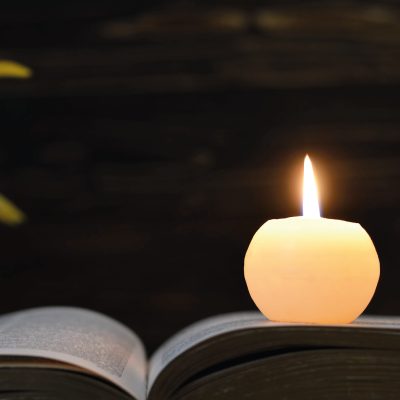 single candle lit placed on an open book